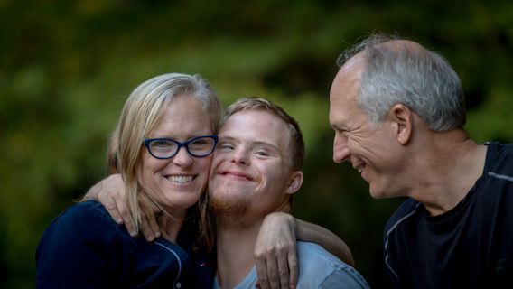 Foto på äldre föräldrar som kramar om sin vuxna son med Downs