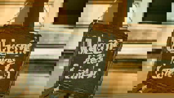 Foto av en griffeltavel-skylt med texten "Welcome please come in", skriven i vitt.