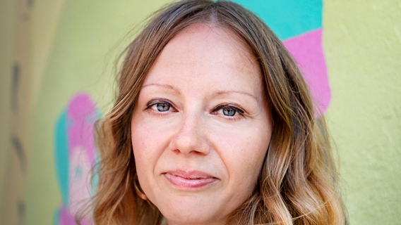 Porträttbild på Paula Tilli med bakgrund som går i gult, turkos och rosa.