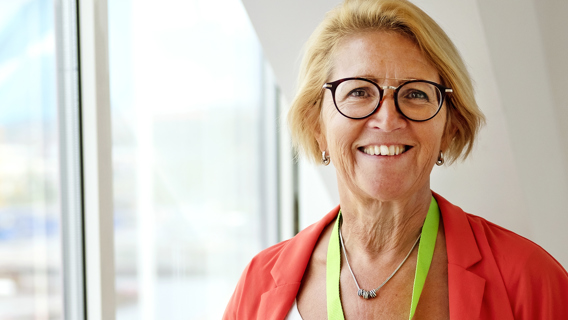 Portättbild på Gunilla Thunberg som står  inomhus vid ett fönster. 