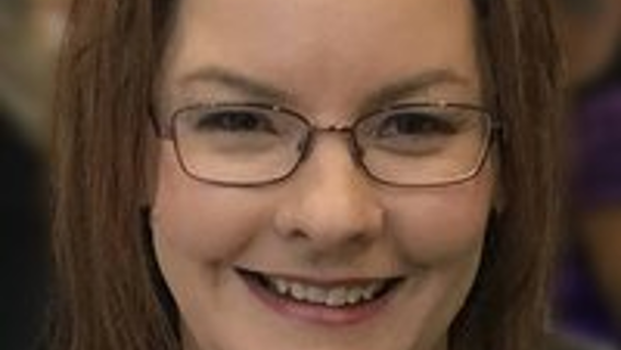 Porträttfoto på Raelene Dundon, leende med brunt axellångt hår i mittbena, rektangulära glasögon